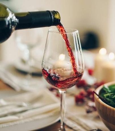 црвено вино које се сипа у чашу за столом