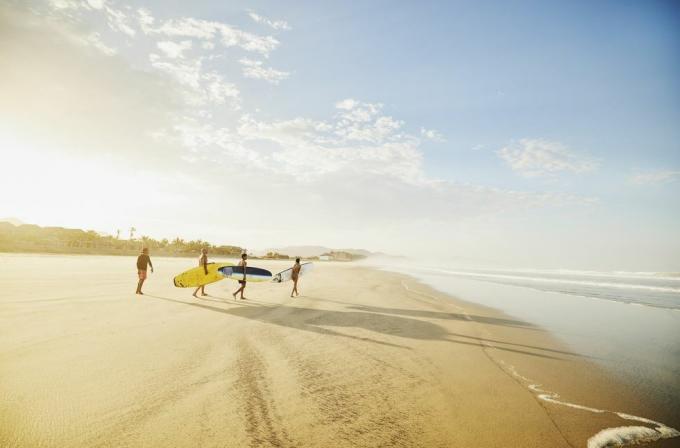 екстремно широки снимак породице која носи даске за сурфовање на тропској плажи док узима часове сурфовања током одмора