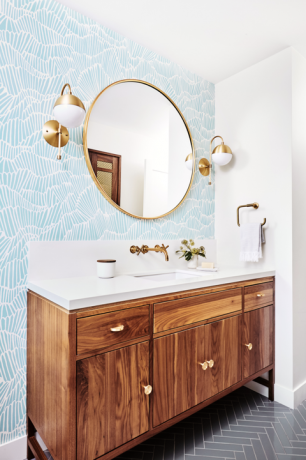 гостињско купатило са светло плавим и белим тапетама у облику шкољке, смеђе ормариће, златно огледало