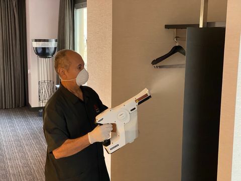 мушкарац у хотелској соби помоћу прскалице за дезинфекцију отвореног ормара